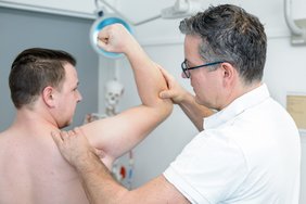 Ein Arzt (rechts im Bild) untersucht die Schulter eines Patienten.