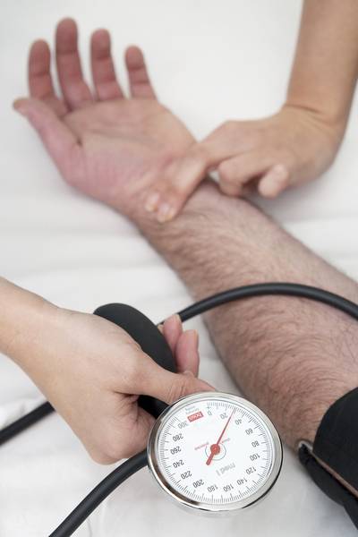 Eine Person misst den Puls und Blutdruck einer anderen Person. Zu sehen sind nur die Hände und die Anzeige des Blutdruckmessgeräts.
