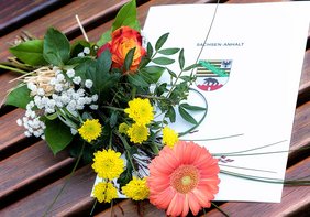 Ein Blumenstrauß liegt auf einem Ausbildungszeugnis mit dem Wappen des Landes Sachsen-Anhalt
