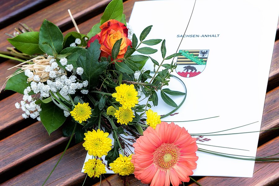 Ein Blumenstrauß liegt auf einem Ausbildungszeugnis mit dem Wappen des Landes Sachsen-Anhalt