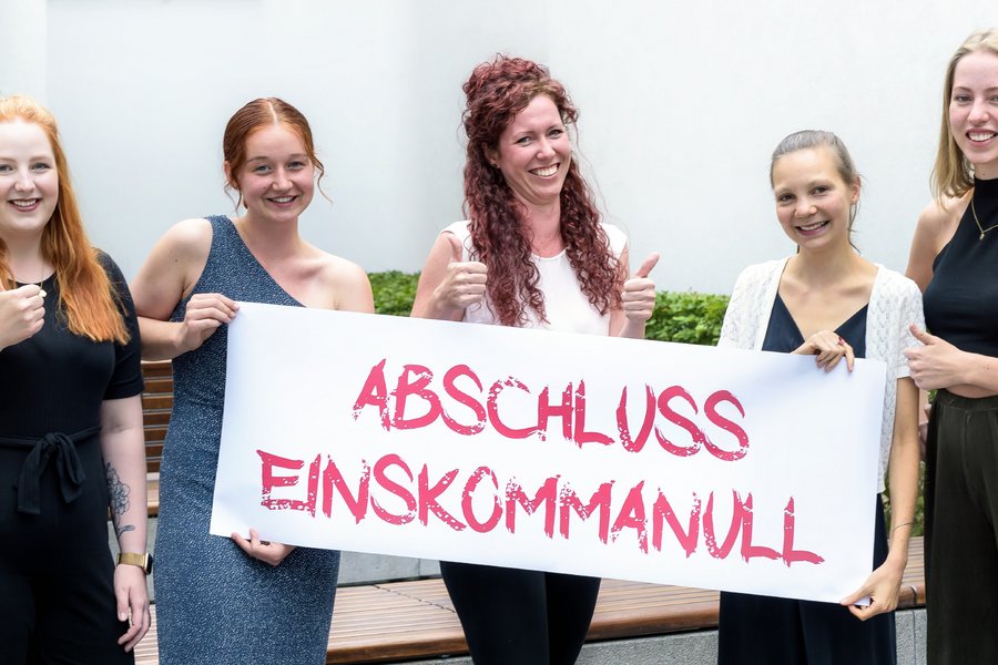 5 junge Frauen stehen nebeneinander und halten ein Banner. Aufschrift: abschluss einskommanull!