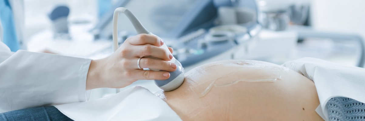 Ultraschallgerät wird von Mediziner:in auf Bauch einer Schwangeren geführt