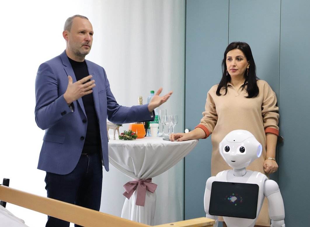 Ein Mann im Jacket erzähl, während ein Roboter und eine Frau im zuhören.