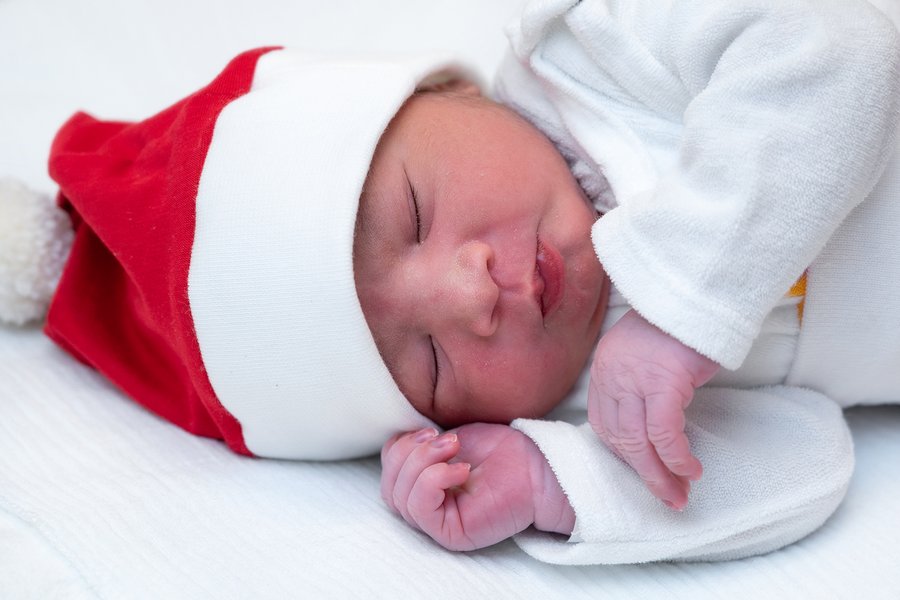 Neugeborenes mit weißer Kleidung und roter Weihnachtsmütze auf der Seite liegend mit geschlossenen Augen