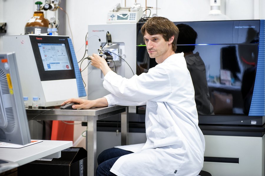 Ein Mann mit weißem Arztkittel sitzt an einem medizinischem Großgerät. Er blickt auf einen Monitor und bedient Regler 