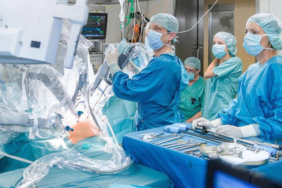 Prof. Dr. Jörg Kleef führt eine Operation mit dem OP-Roboter Da Vinci durch. Er ist umgeben von Mitarbeiterinnen und Mitarbeitern in OP-Kleidung. Alle schauen auf einen Bildschirm oben links im Bild.