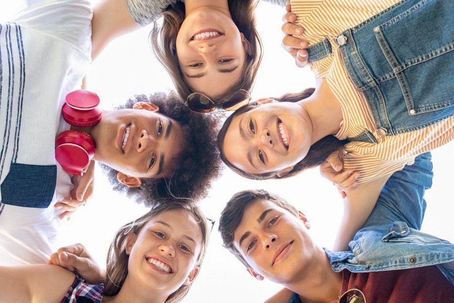 The camera is on the ground and is pointing towards the sky. Five young people stretch their heads into the picture.  The camera is on the ground and is pointing towards the sky. Five young people stretch their heads into the picture.
