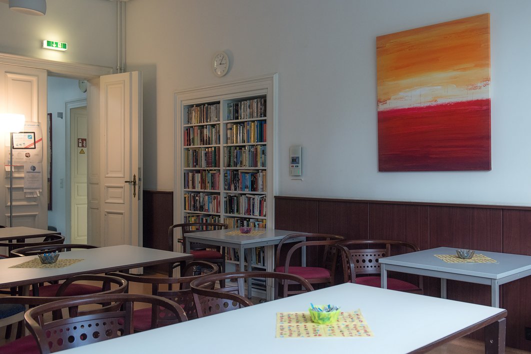 Blick in einen Raum mit Tisch, Stühlen, Bücherregal und Bild an der Wand