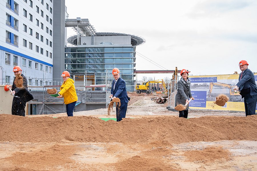 Fünf Menschen beim Spatenstich für neues Gebäude der Universitätsmedizin Halle (Saale). Im Hintergrund ist das Hauptgebäude des Universitätsklinikum zu sehen.