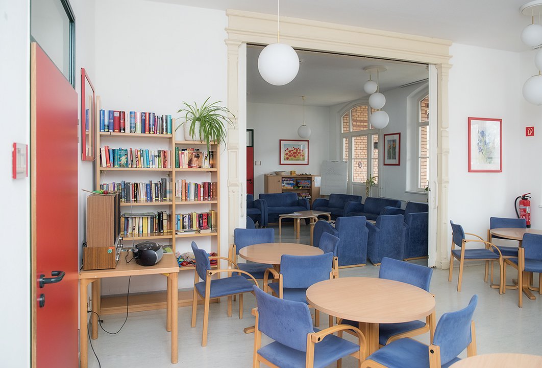 Raum mit Bücherregalen, Tischen und blauen Sesseln