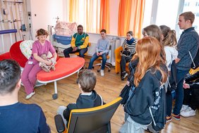 Eine Gruppe von Schüler:innen steht im Kreißsaal des Universitätsklinikums Halle (Saale). Hebamme Astrid Dening erklärt den Schüler:innen die Abläufe und den Geburtsvorgang.