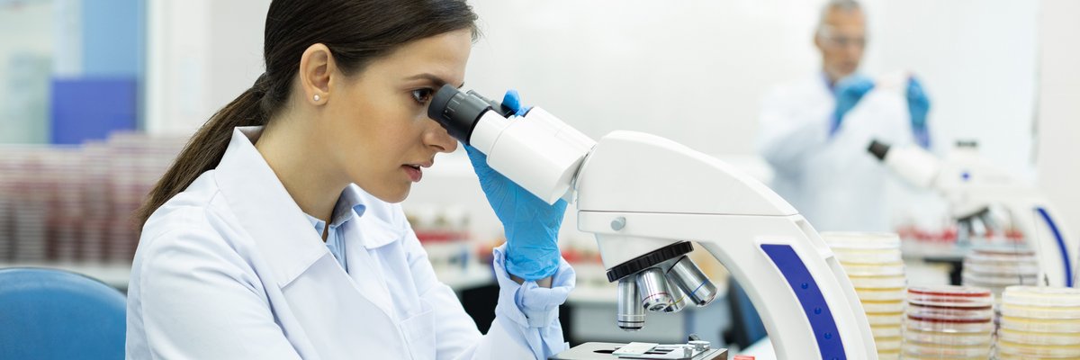 Frau arbeitet am Mikroskop, weiterer Mensch im Hintergrund