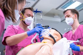 Medizinisches Personal in Arbeits- und Schutzkleidung beatmet eine Simulationspuppe.
