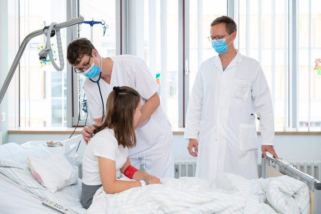 Zwei Ärzte am Krankenhausbett eines Mädchens. Das Kind wird mit einem Stetoskop abgehört