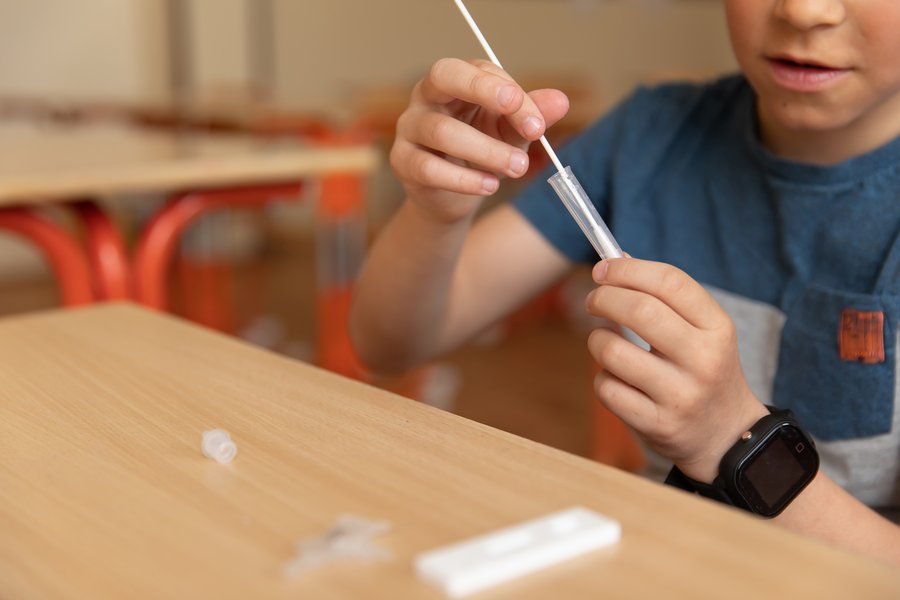 Ein Schulkind führt einen Corona-Antigen-Schnelltest in der Schule durch. Das Kind steckt gerade den Tupfer in das Röhrchen mit der Lösung, vor ihm auf dem Tisch liegen die anderen Test-Utensilien.