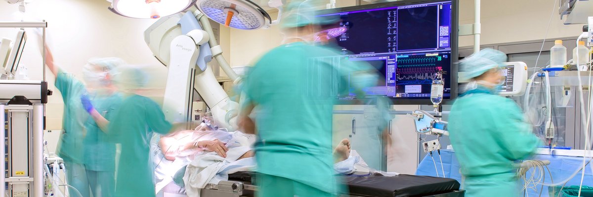 Operationssituation. Mitarbeitende kümmern sich um den Patienten und checken die Werte an den Geräten und Computern.