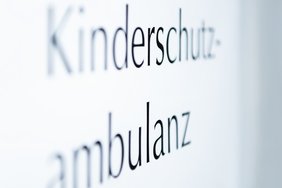 auf weißem Hintergrund steht zweizeilig das Wort Kinderschutz-ambulanz. Teile der Schrift sind verschwommen.