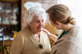 Eine jüngere Frau rechts im Bild spricht liebevoll mit einer älteren Frau links im Bild.