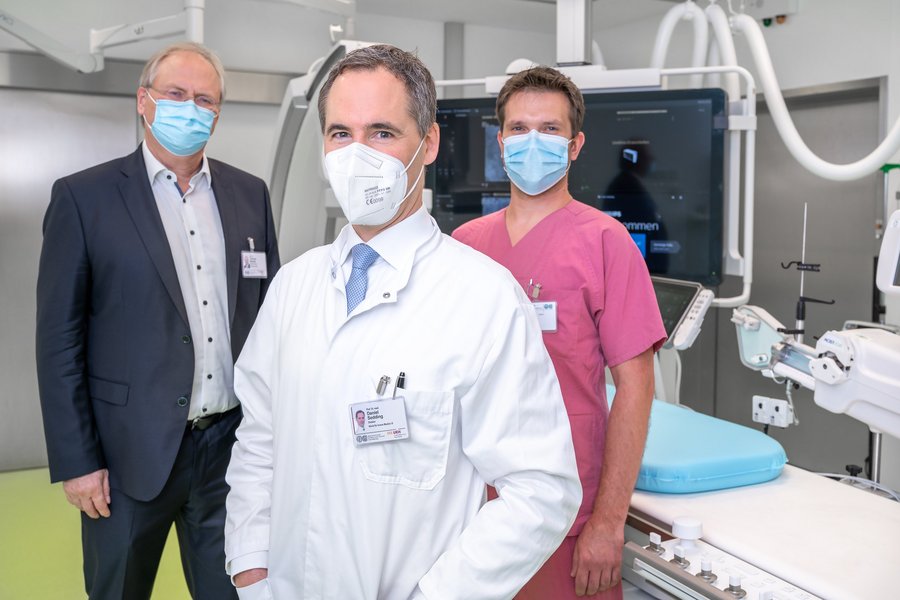 Drei Männer vor einem Herzkatheter-Messplatz. Es ist ein Monitor im Hintergrund zu sehen  Drei Männer vor einem Herzkatheter-Messplatz. Es ist ein Monitor im Hintergrund zu sehen