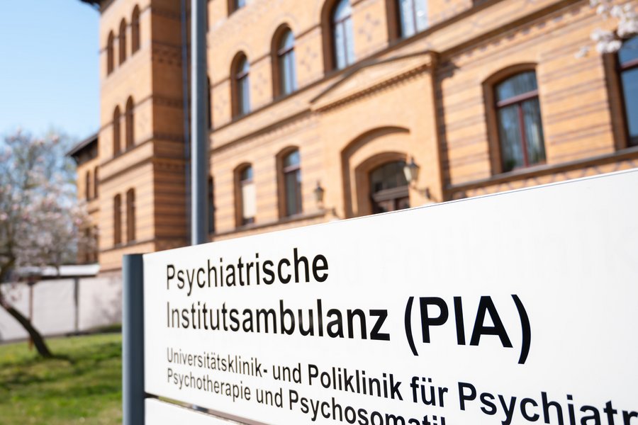 Vor einem Backsteingebäude steht ein Hinweisschild. Darauf steht Psychiatrische Institutsambulanz (PIA)