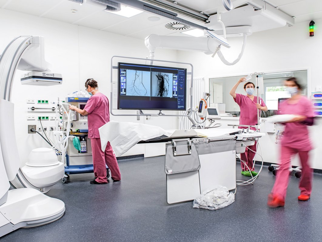 Behandlungsraum der Radiologie mit medizinischen Geräten und drei Beschäftigten