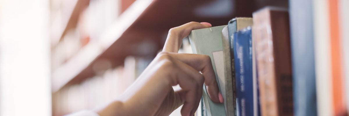 Ein Mensch nimmt ein Buch aus einem Bücherregal, ist es eine Hand zu sehen