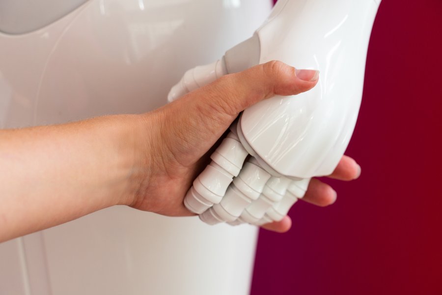 Ein Roboter und ein Mensch halten sich an der Hand.